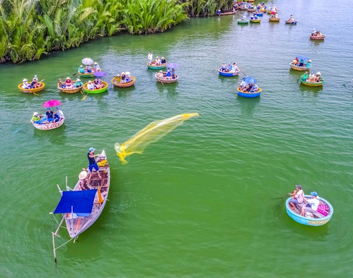 Aerial view of Hoi An fishing net activity with round boats on green water.