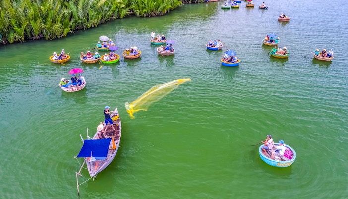 Aerial view of Hoi An fishing net activity with round boats on green water.