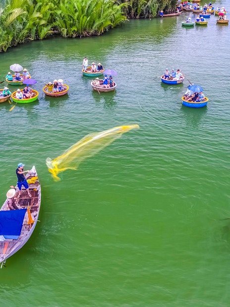 Aerial view of Hoi An fishing net activity with round boats on green water.
