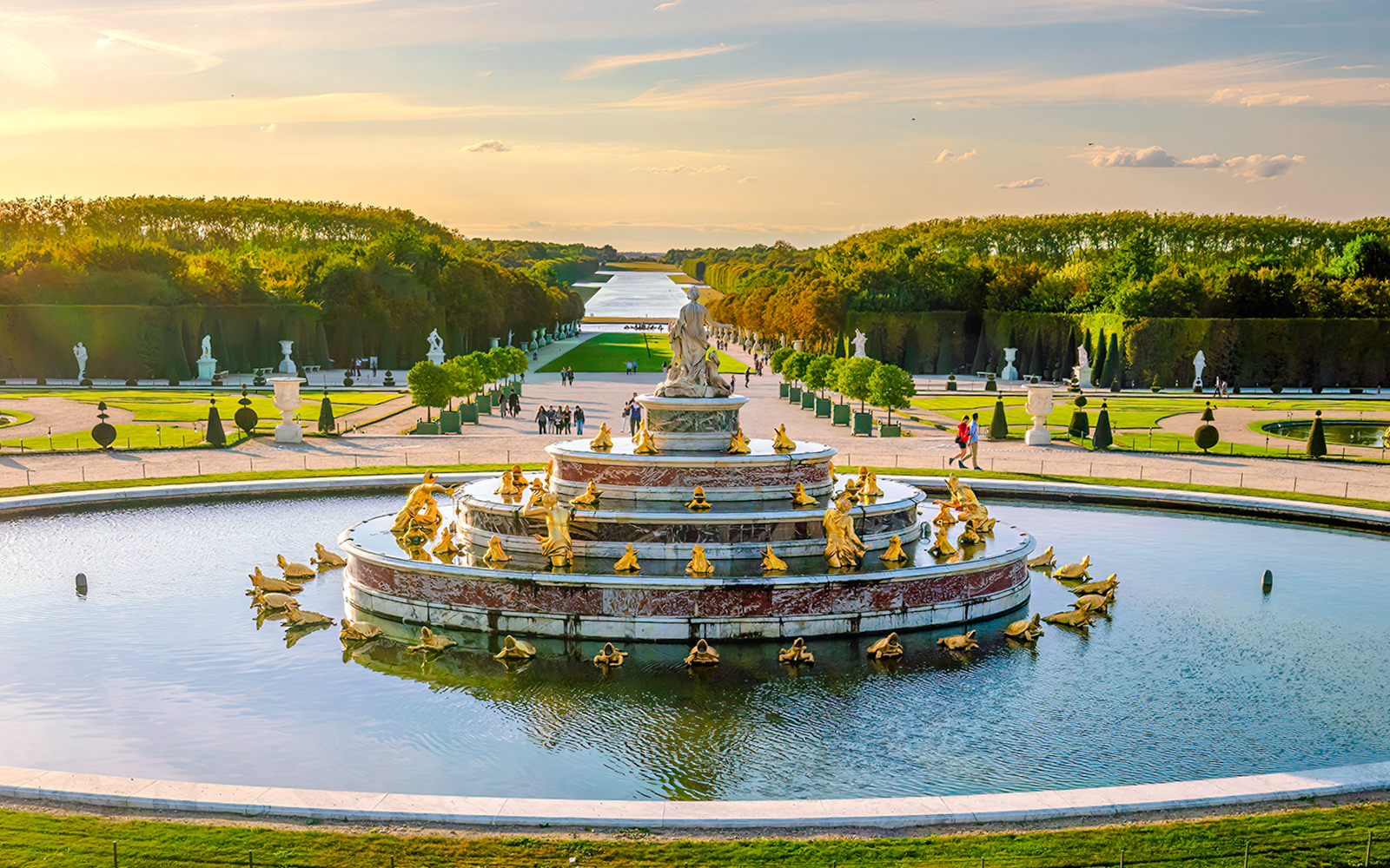 Fountain at Versailles Palace with golden statues and gardens in the background.