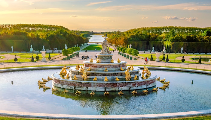 Fountain at Versailles Palace with golden statues and gardens in the background.