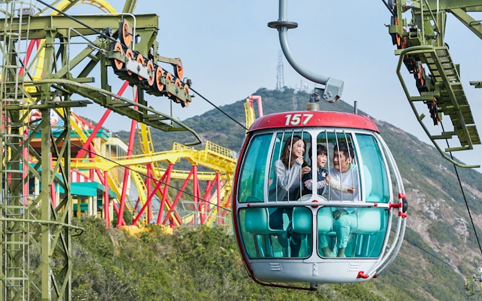 Cable car ride at Ocean Park with family enjoying views of amusement rides and mountains.