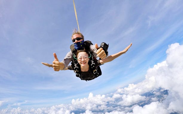 Skydiving tandem over Pattaya with female tourist smiling above clouds.