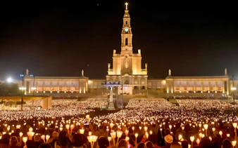 Candlelight procession at Fátima Sanctuary, Portugal, with a large crowd holding candles at night.