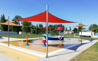 Outdoor pool with colorful shades and play structures at Pesterzsebet Bath, Budapest.