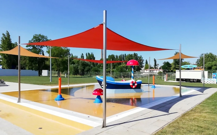 Outdoor pool with colorful shades and play structures at Pesterzsebet Bath, Budapest.