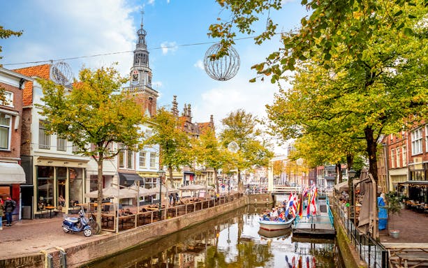 Canal view with boat tour in Altstadt, Alkmaar, Netherlands, featuring historic buildings and church tower.