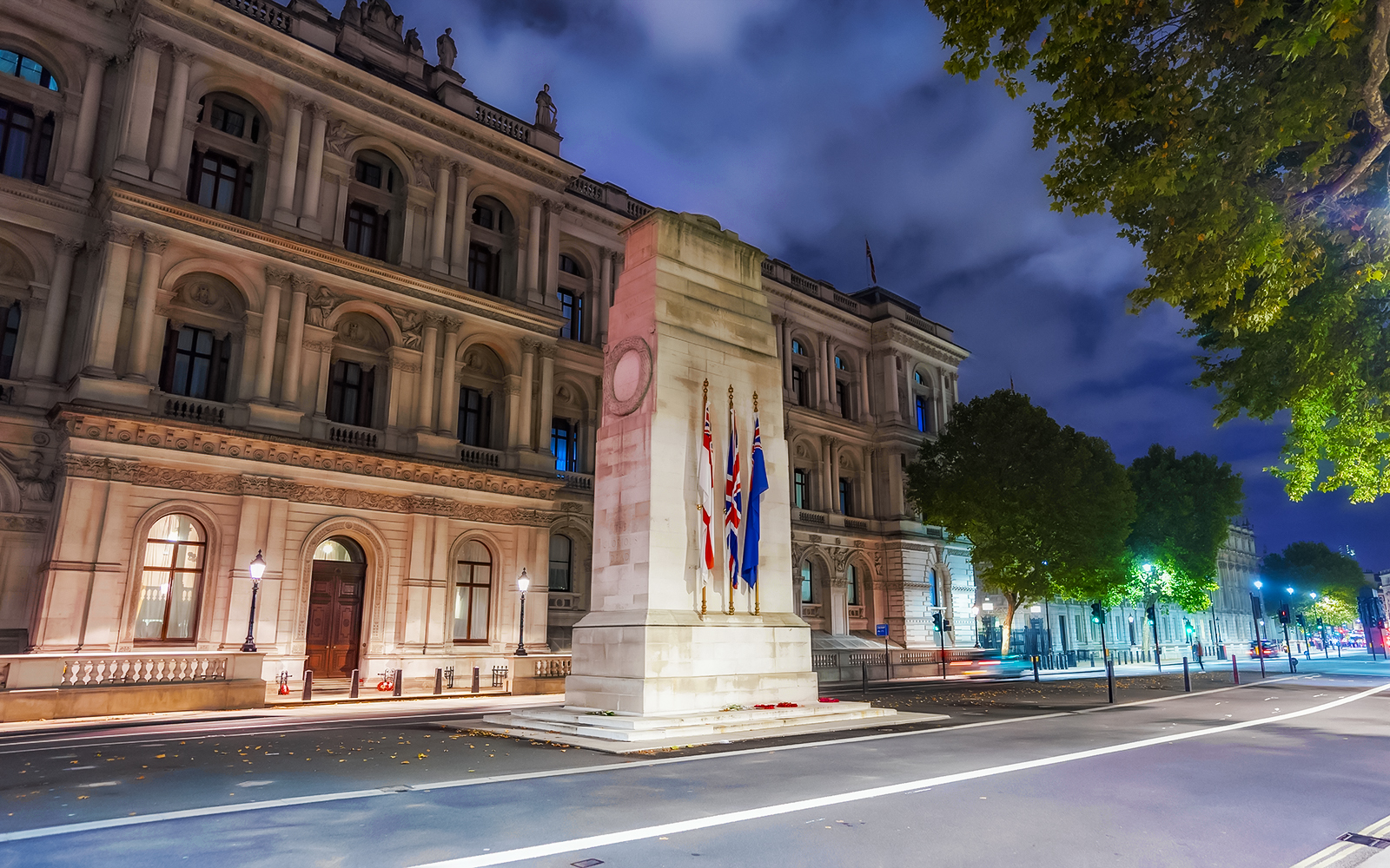 Cenotaph memorial with flags in Whitehall, London illuminated at night.