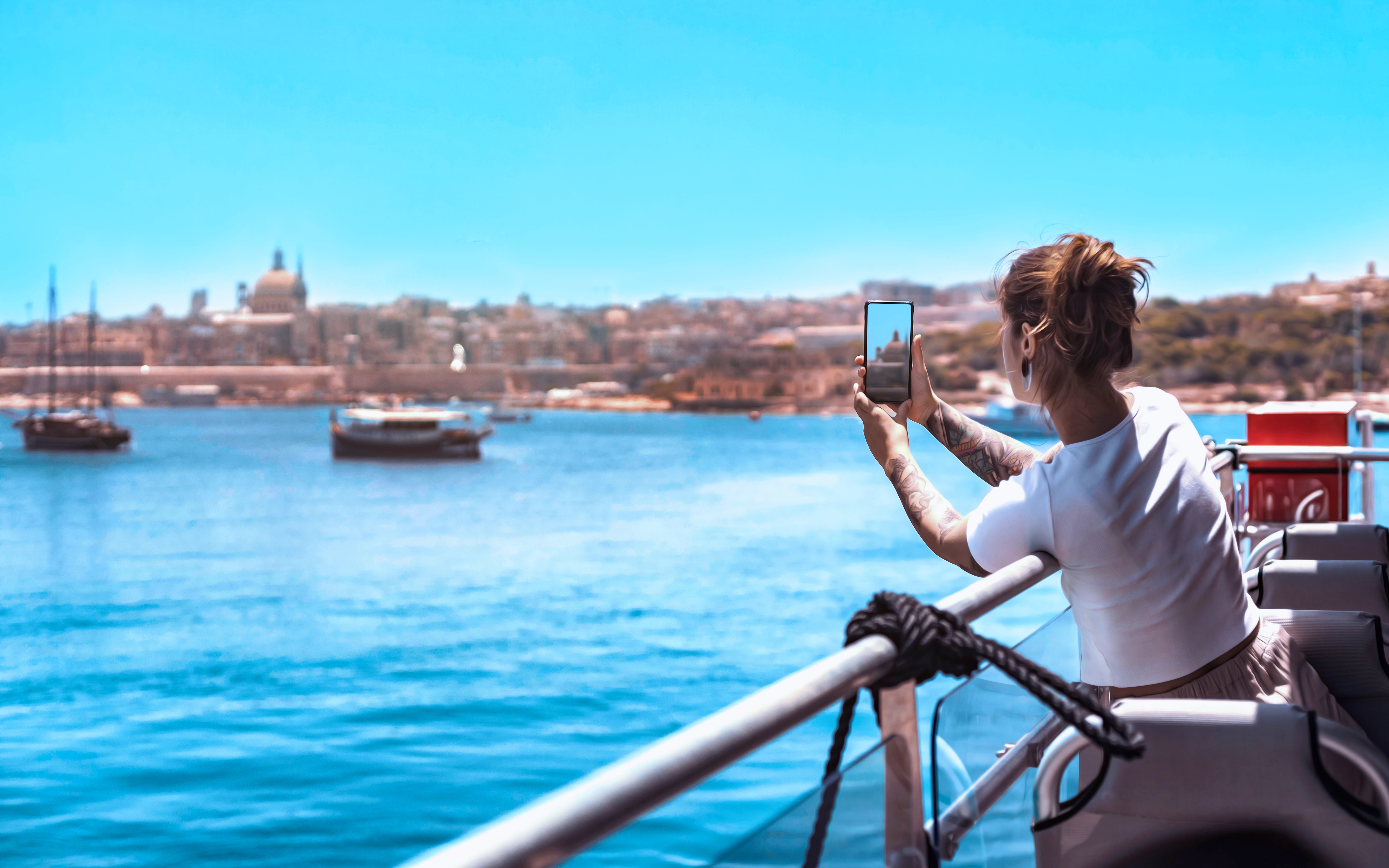 Person taking photo on harbour cruise with cityscape view in background.