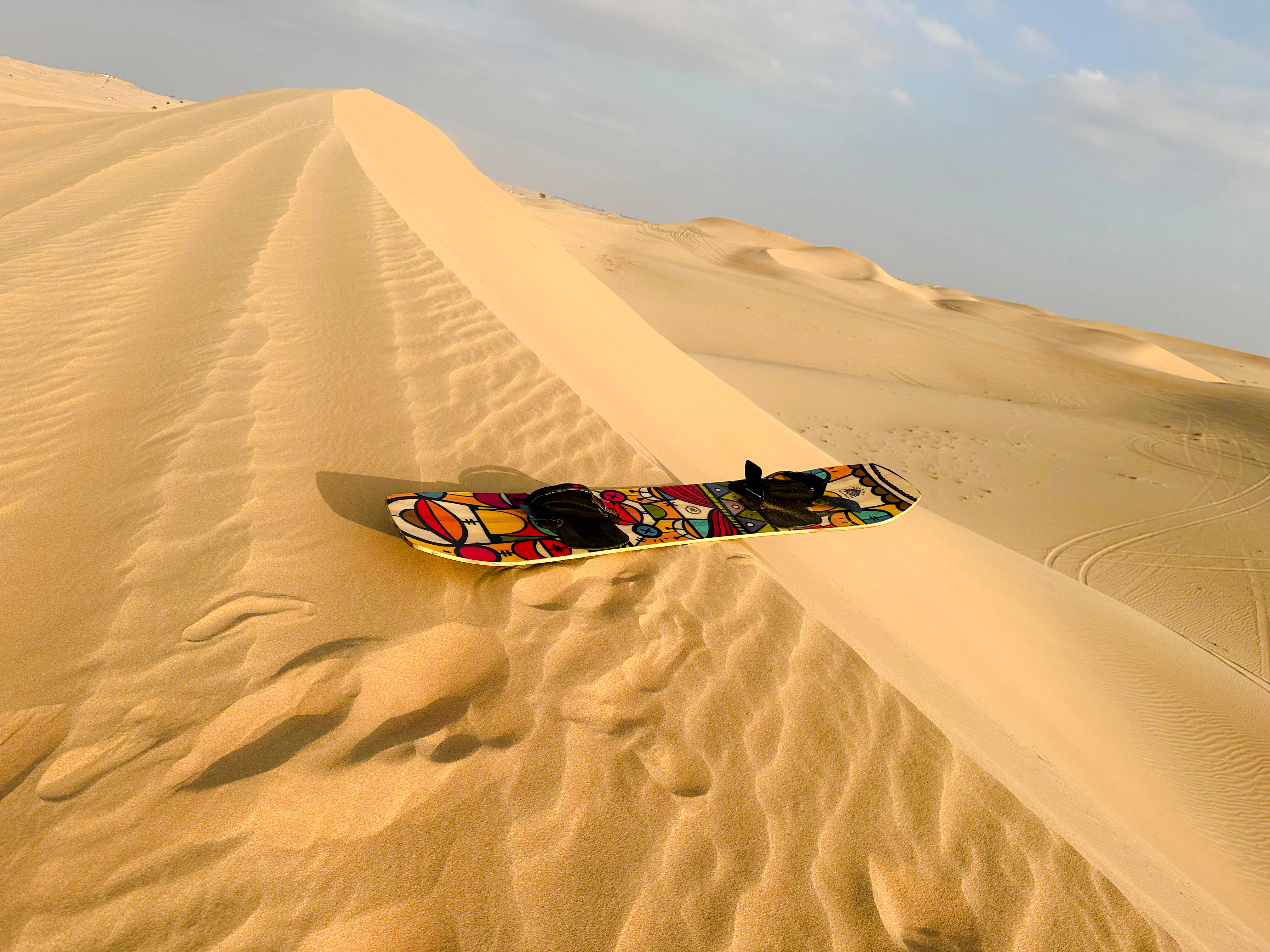 Sandboard on a dune during Abu Dhabi morning desert safari with sandboarding and camel ride.