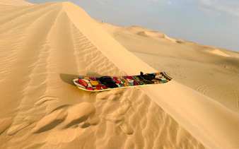 Sandboard on a dune during Abu Dhabi morning desert safari with sandboarding and camel ride.
