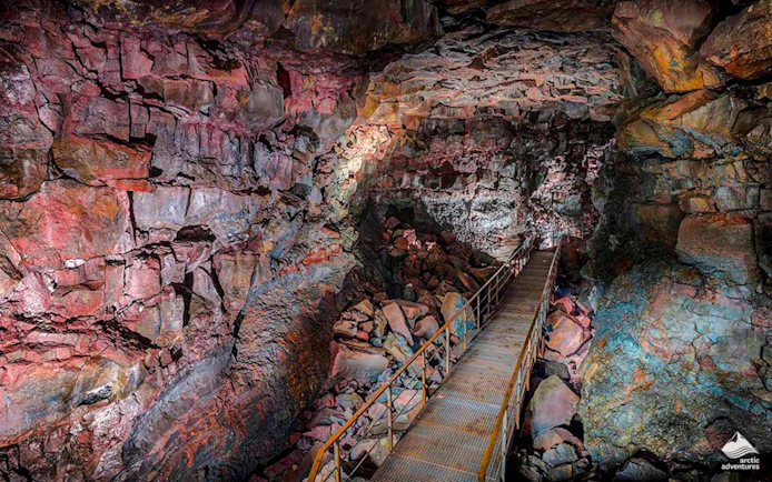 Raufarhólshellir Lava Tunnel interior with walkway and colorful rock formations.