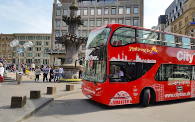 Hop on Hop off City Tour bus in Cologne near historic fountain.