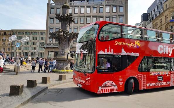 Hop on Hop off City Tour bus in Cologne near historic fountain.