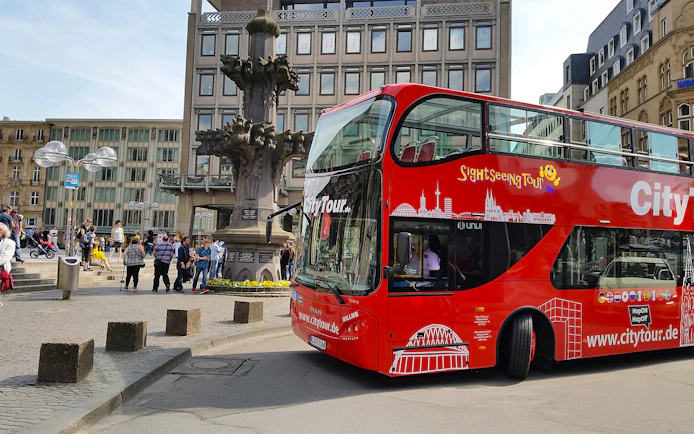Hop on Hop off City Tour bus in Cologne near historic fountain.