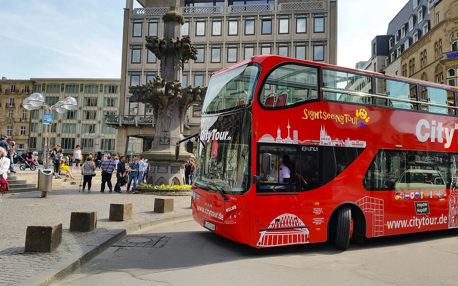 Hop on Hop off City Tour bus in Cologne near historic fountain.