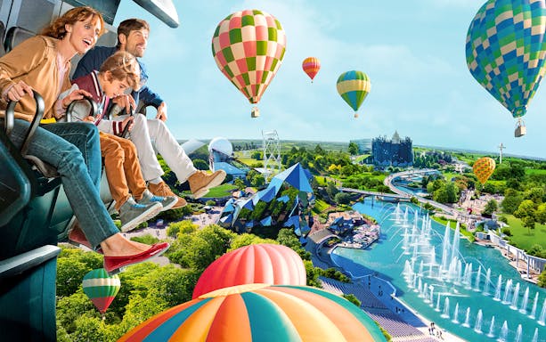 Family enjoying a ride with hot air balloons and futuristic architecture at Futuroscope, France.