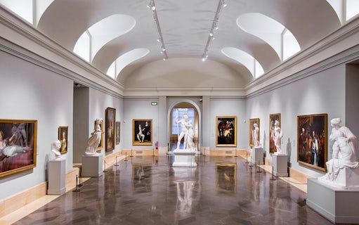 Interior of Prado Museum gallery with classical sculptures and paintings.