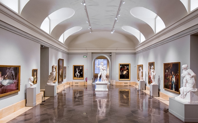 Interior of Prado Museum gallery with classical sculptures and paintings.