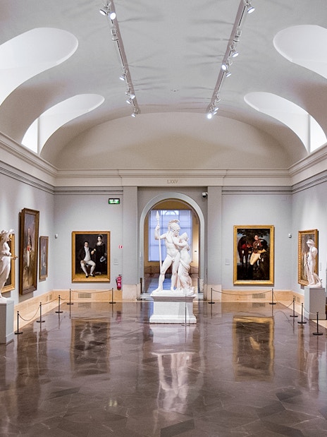 Interior of Prado Museum gallery with classical sculptures and paintings.