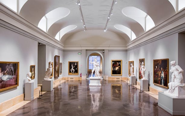 Interior of Prado Museum gallery with classical sculptures and paintings.