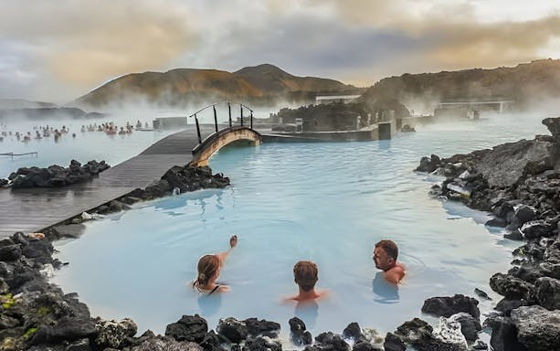 People relaxing in the Blue Lagoon geothermal spa with misty volcanic landscape, Iceland.
