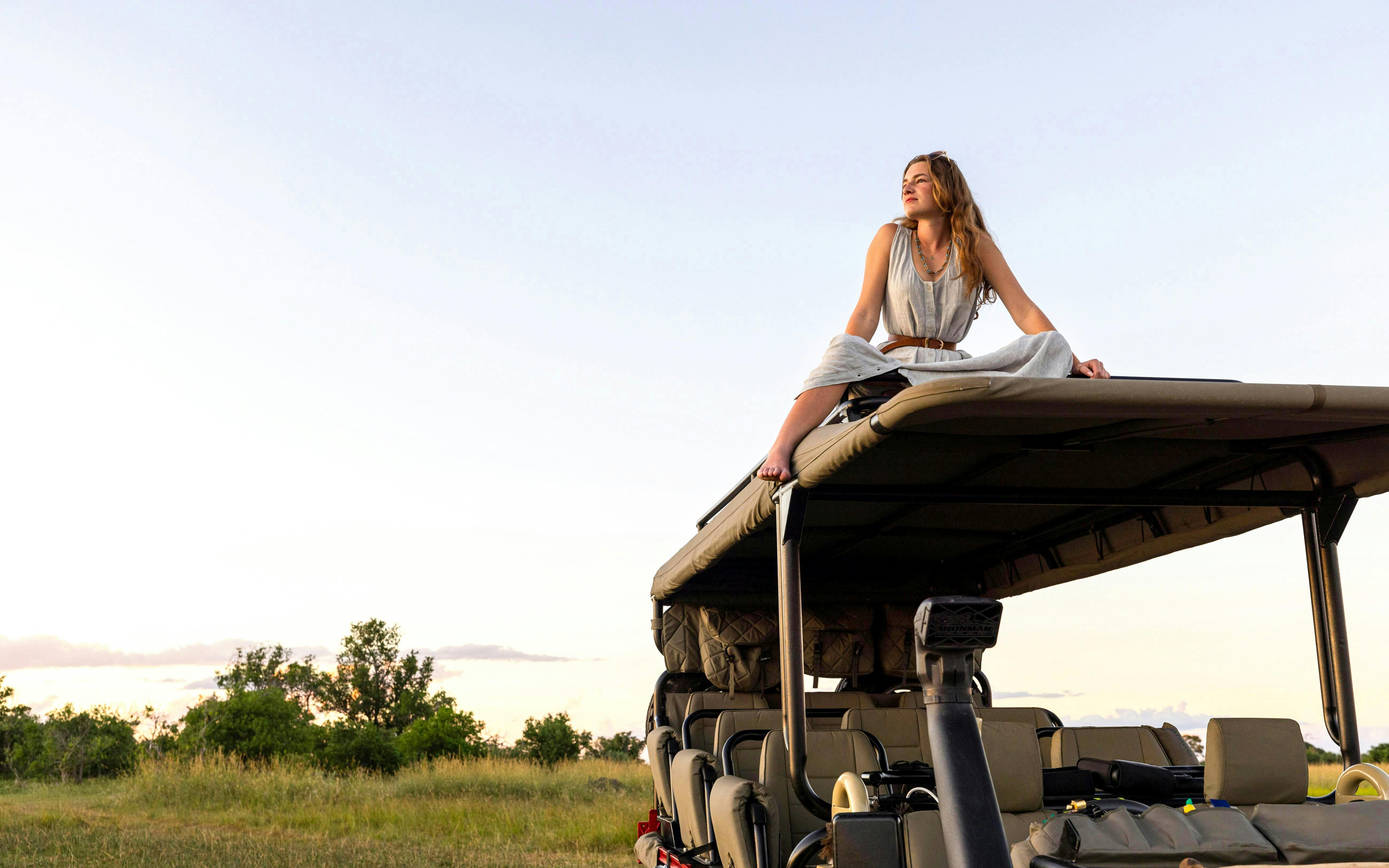 Girl sitting on safari vehicle roof in African savanna.