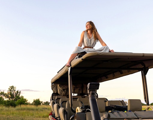 Girl sitting on safari vehicle roof in African savanna.