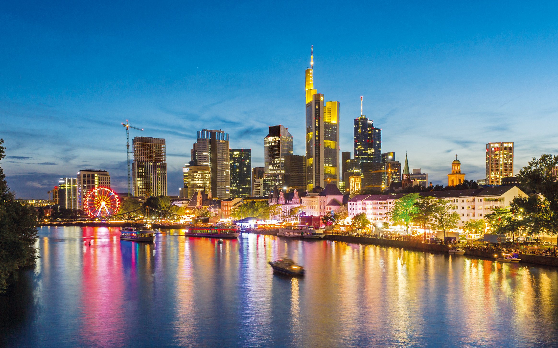 Frankfurt skyline at night with illuminated buildings and river reflections.