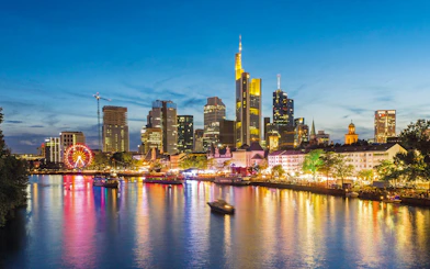 Frankfurt skyline at night with illuminated buildings and river reflections.