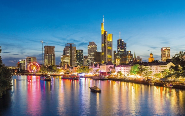 Frankfurt skyline at night with illuminated buildings and river reflections.
