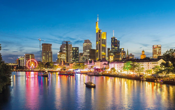 Frankfurt skyline at night with illuminated buildings and river reflections.