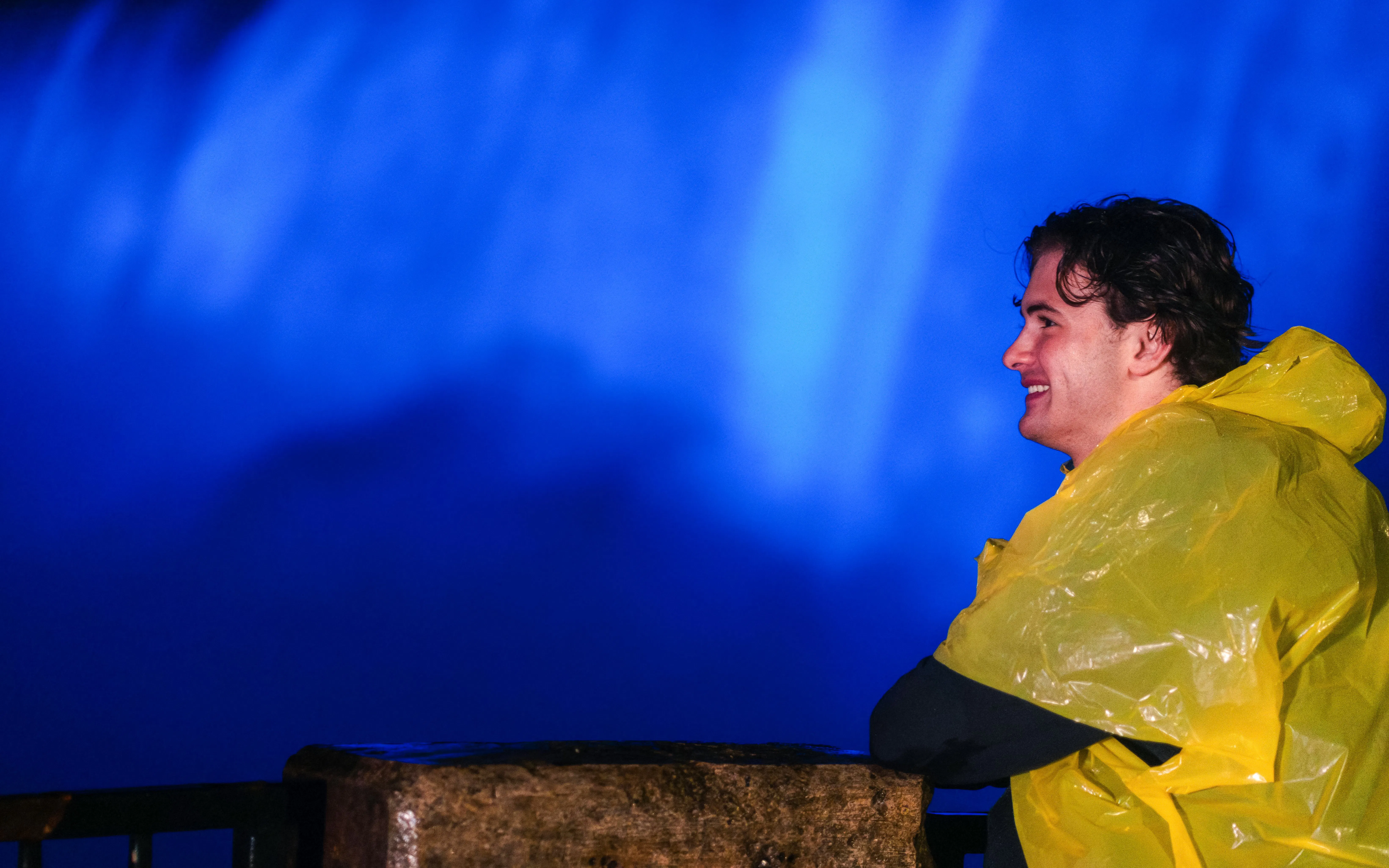 Person in yellow poncho enjoying Niagara Falls illuminated at night.