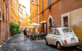 Cobblestone street in Trastevere, Rome with outdoor café and vintage car.