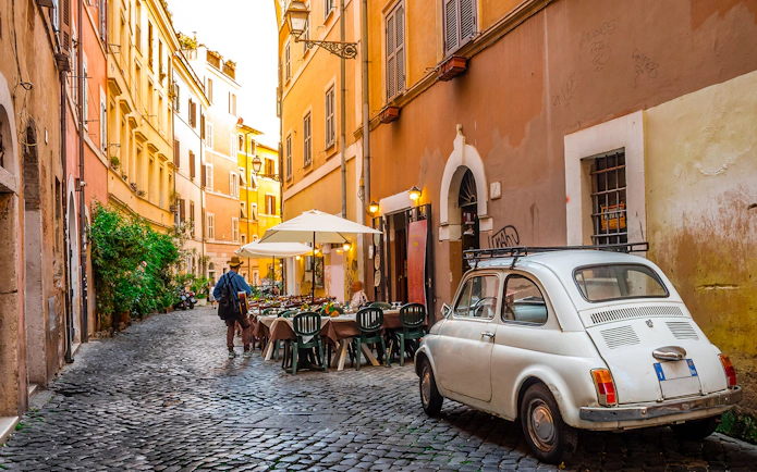 Cobblestone street in Trastevere, Rome with outdoor café and vintage car.