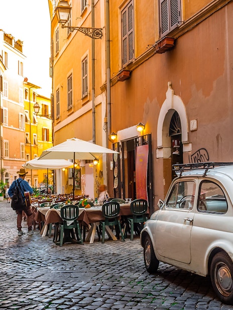 Cobblestone street in Trastevere, Rome with outdoor café and vintage car.