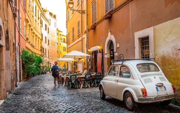 Cobblestone street in Trastevere, Rome with outdoor café and vintage car.