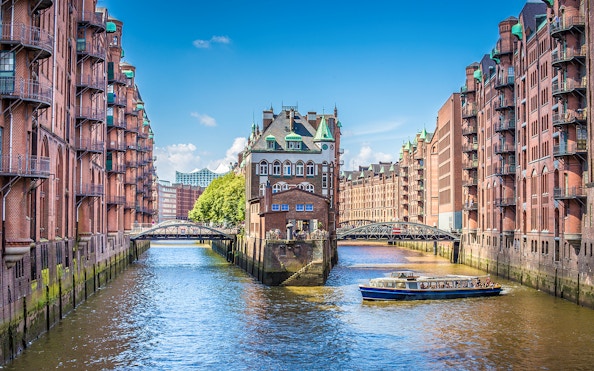 Boat cruising through Hamburg's Speicherstadt canal with historic brick warehouses.