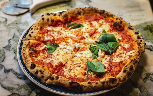 Pizza with basil leaves served on a marble table in Florence.