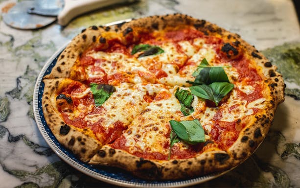 Pizza with basil leaves served on a marble table in Florence.