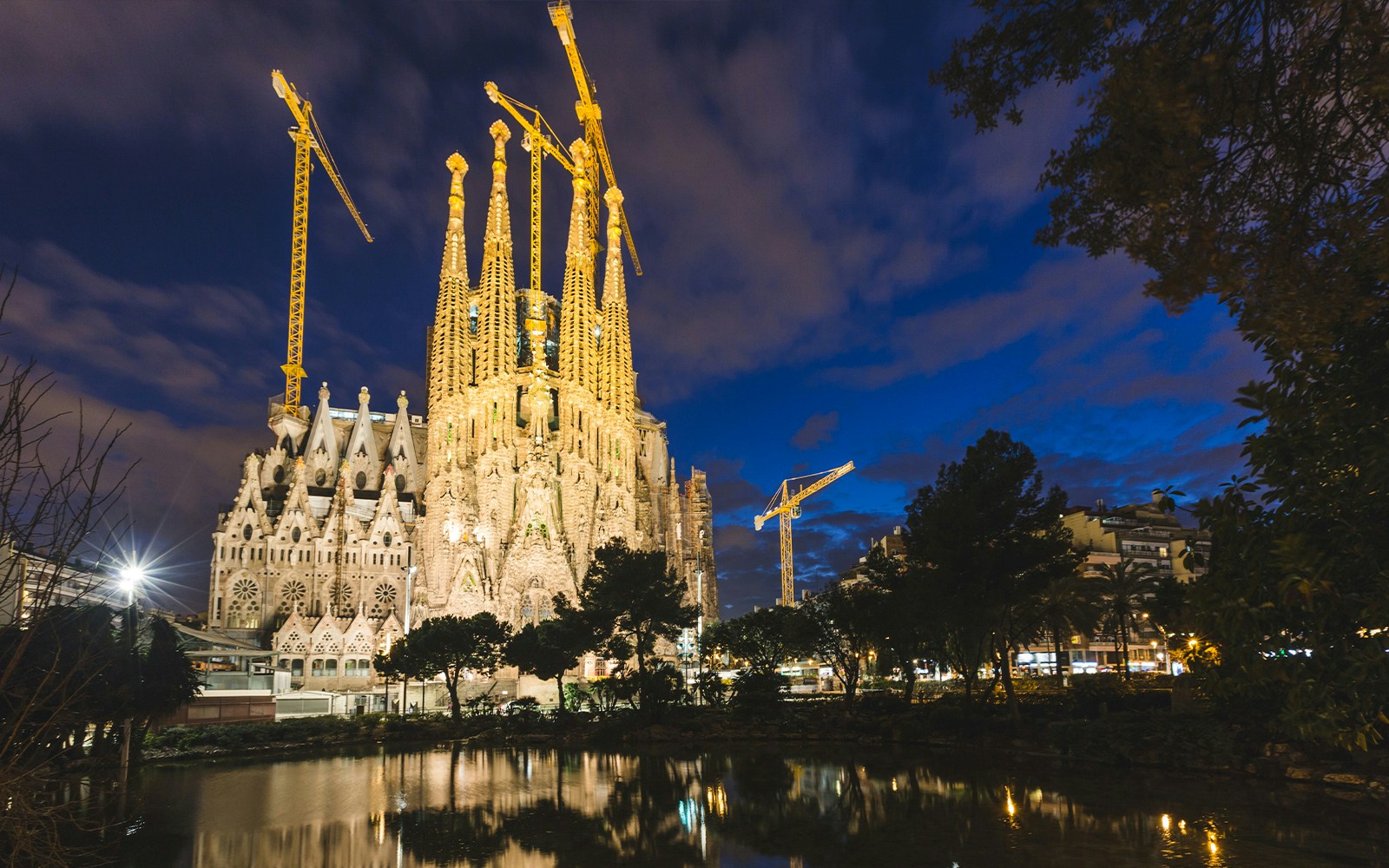 Sagrada Familia illuminated at night in Barcelona with cranes in the background.