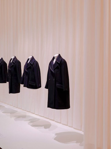 Coats displayed at Martin Grant Exhibition with framed artwork on the wall.