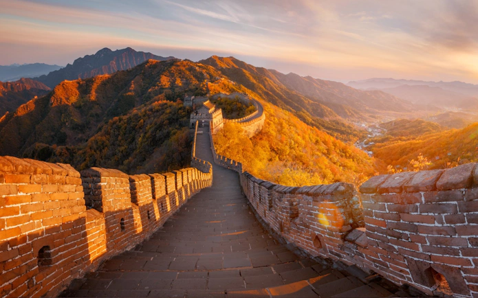Great Wall of China at sunrise with mountains in the background.