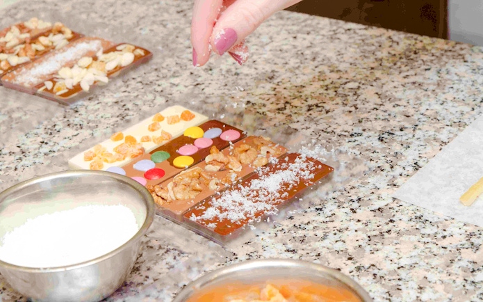 Hand decorating chocolate bars with nuts and candies at Choco-Story Paris.