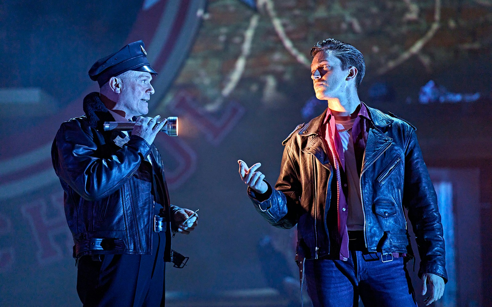 Two actors in leather jackets perform a scene from the musical "Grease" on stage.
