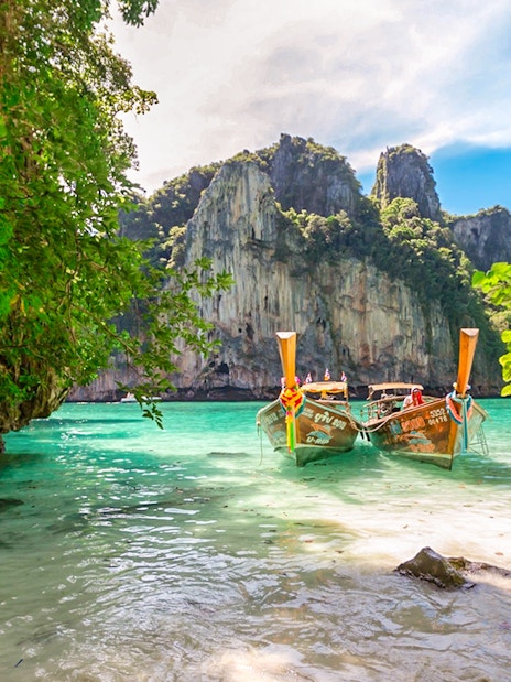 Longtail boats on Maya Bay beach, Bamboo Island, Phi Phi with limestone cliffs.