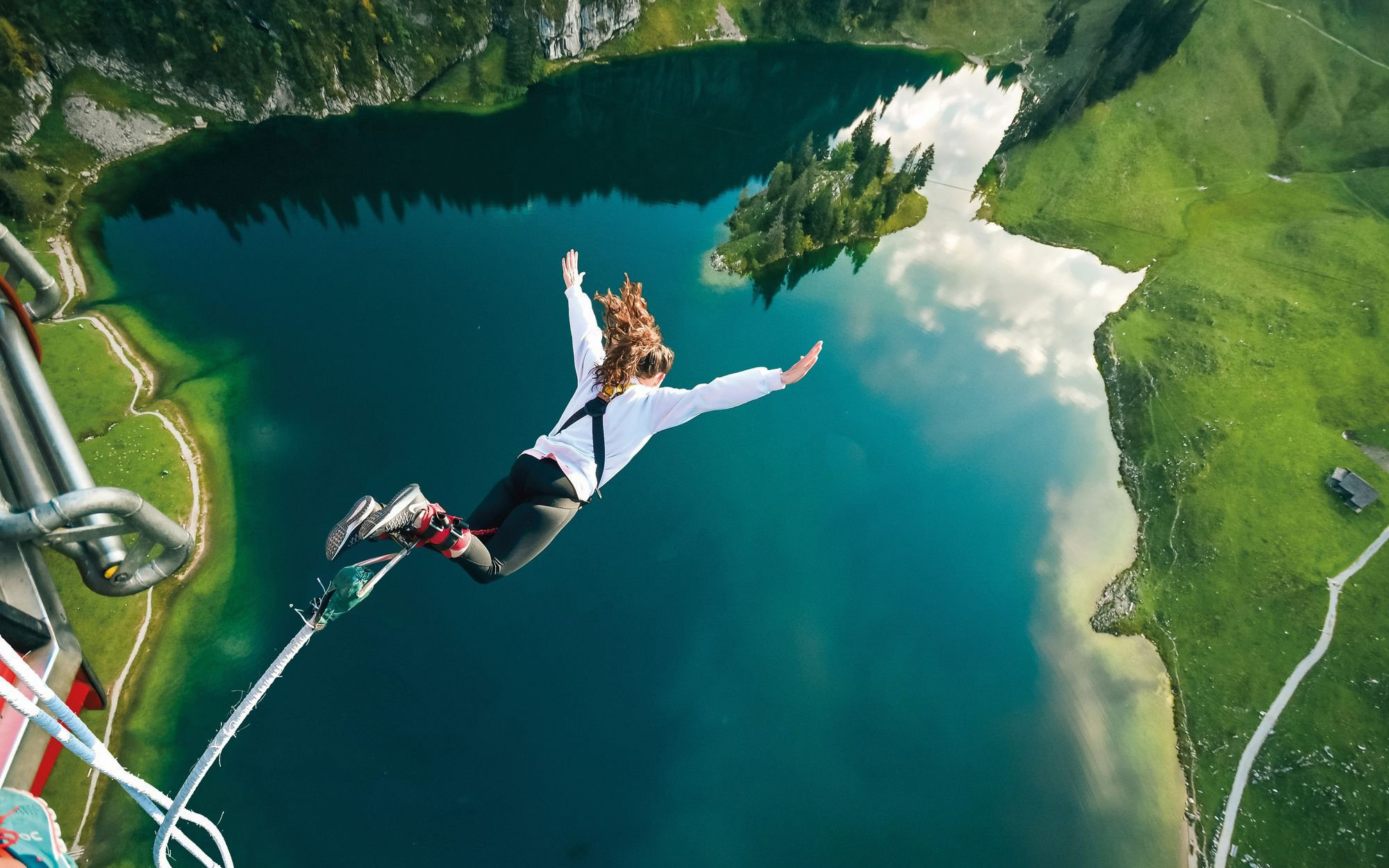 Person bungee jumping over Stockhorn Lake, Interlaken, surrounded by lush green landscape.