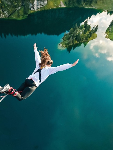 Person bungee jumping over Stockhorn Lake, Interlaken, surrounded by lush green landscape.