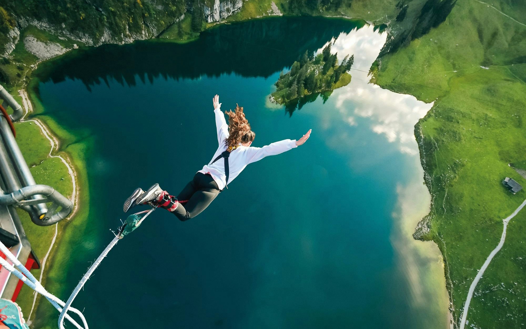 Person bungee jumping over Stockhorn Lake, Interlaken, surrounded by lush green landscape.