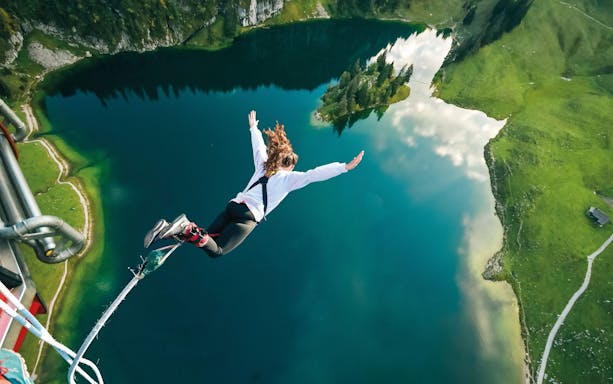 Person bungee jumping over Stockhorn Lake, Interlaken, surrounded by lush green landscape.